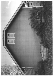 Sort-hvitt fotografi av en bygning sett fra siden, som viser fasaden, vinduer, tak og omgivelsene.