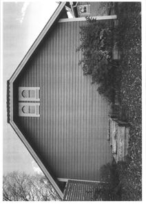 Sort-hvitt fotografi av en bygning sett fra siden, som viser fasaden, taklinjen, vinduer og omgivelsene.