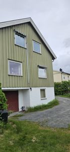Fotografi av en grønn og hvit villa sett fra siden, med synlig fasade, vinduer, tak og omgivelser.