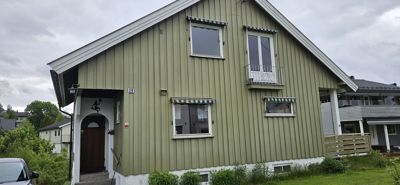 Fotografi av fasaden på en grønn, toetasjes villa med vinduer, balkong og inngang.