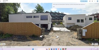 Fotografi av en nybygd hvit bolig med en grusvei og en gateoppføring i forgrunnen.