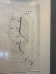 En tegning som viser fasaden (framsiden) av en planlagt bygning, inkludert vinduer, tak og omgivende beplantning.