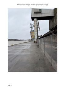 Fotografi av en industriell bygning ved vannet, med en heis (elevator) og en gjerde i forgrunnen.