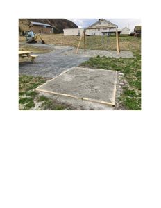 Fotografi av en utendørs byggeplass med en nybetont betongplate, en svingbåstasjon og eksisterende hus i bakgrunnen.