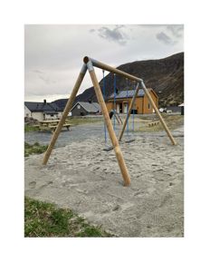Fotografi av en utelekeplass med en sving, et bord og en bygning i bakgrunnen.