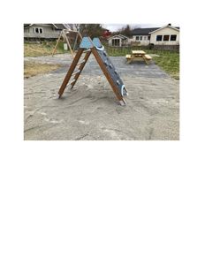 Fotografi av en utendørs lekapparat (en A-formet klatrestige) på en sandplass, med hus i bakgrunnen.