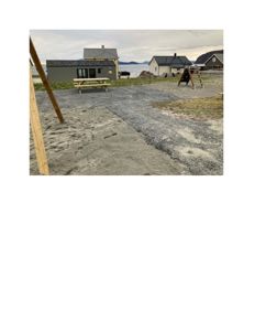 Fotografi av en byggeplass eller et område med flere hus, en nybygd grå bygning, og utstyr som en bordbenk og en trapp.