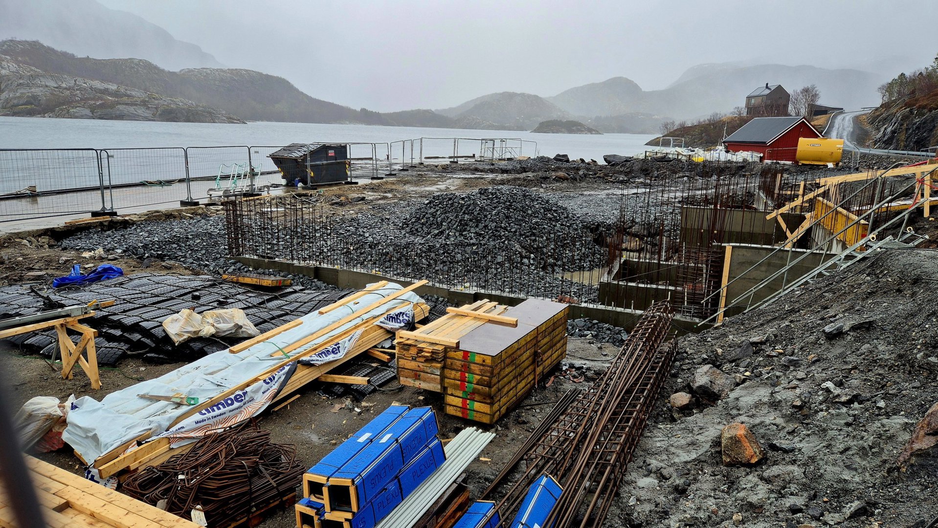 Fotografi av et byggeplass ved vannet med grunnarbeider i gang, inkludert armering og materialer.