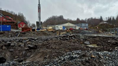 Fotografi av et byggeplassområde med graving, maskiner og nabolag i bakgrunnen.