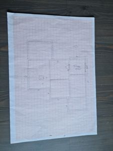 En håndtegnet etasjeplan (plantegning) på millimeterpapir som viser romfordeling, vegger og dimensjoner.