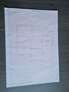 En håndtegnet etasjeplan (plantegning) på millimeterpapir som viser romfordeling, vegger og dimensjoner.