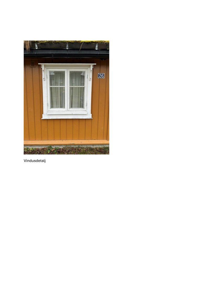 Fotografi av en vindusdetalj på en gulemalt fasade med hvit ramme og tak med mos.