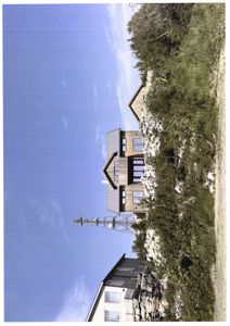 Fotografi av en bygning i tre med et tak, sett fra siden mot en blå himmel og vegetasjon.