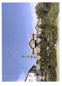 Fotografi av en bygning sett fra siden, med en steinmur og vegetasjon i forgrunnen.