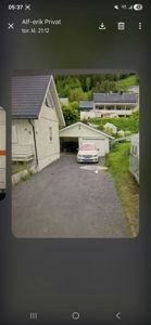 Fotografi av en bolig med garasje og kjørevei sett fra nede i terrenget.