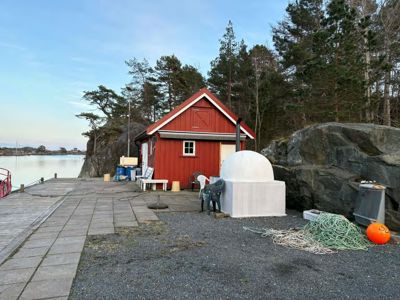 Fotografi av en rød hytte ved vannet med en hvit, kuppelformet struktur foran.