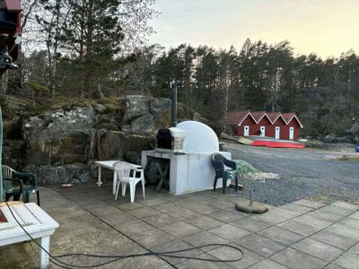 Fotografi av en uteplass med en pizzaovn, møbler og en rød uthusbygning i bakgrunnen.