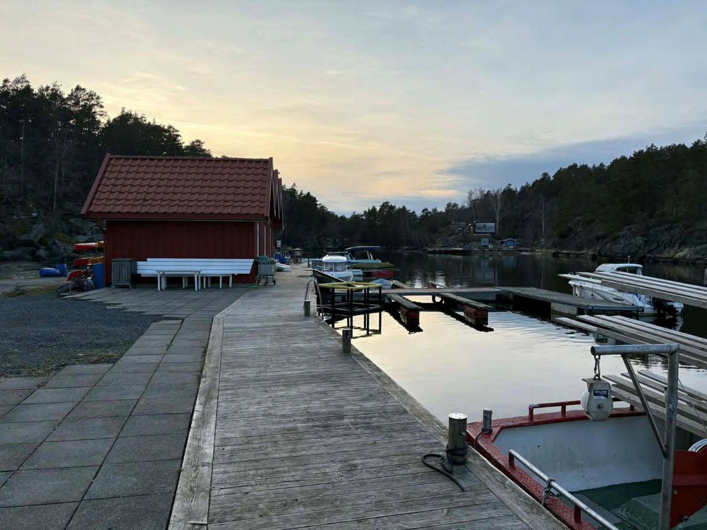 Fotografi av en rød bygning ved en kai med båter og en havn i bakgrunnen.