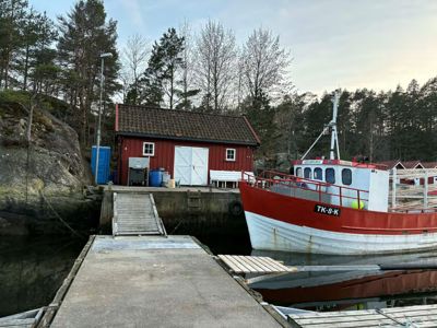 Fotografi av en rød båthavn med en båt og en liten uthusbygning.