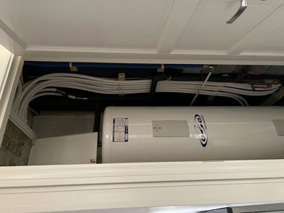 Fotografi av en varmtvannsbereder og tilhørende rørlegging i et teknisk rom eller skap.