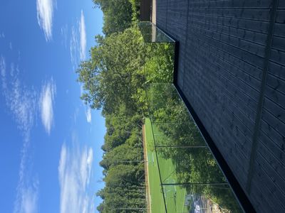 Fotografi av en moderne fasade med mørke trepanel og glassvegg, sett fra utsiden mot en grønn idrettsbane.