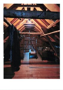 Fotografi av et innendørs rom, sannsynligvis et loft eller etasjens overste del, med synlige trebjelker og møbler.