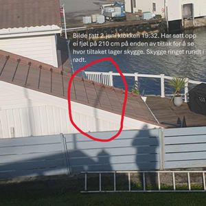 Fotografi av en bygning med tak, hekk og en del av en kai eller brygge i bakgrunnen. Bildet inneholder også en tekstbeskrivelse og en håndtegnet sirkel.