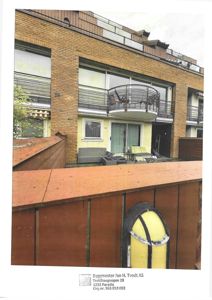 Fotografi av en eksisterende bygning sett fra bakgårdssiden, med balkonger, terrasse og utemøbler synlig.