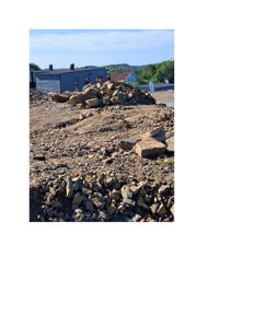 Fotografi av et byggefelt med steinmasser i forgrunnen og en blå bygning i bakgrunnen.