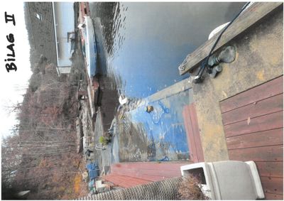 Fotografi av en kai eller brygge ved vann, med båter og en bygning i bakgrunnen.