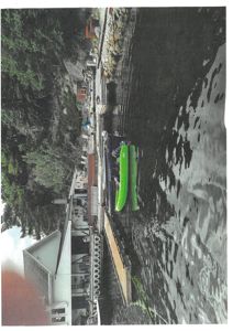 Fotografi av en bygning ved vannet med en brygge og en båt.