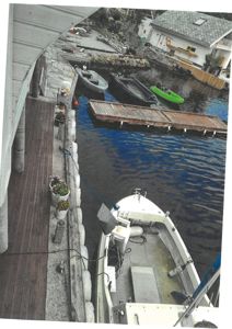 Fotografi av en brygge med båter, en kai og en bygning i bakgrunnen.