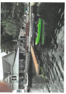 Fotografi av en brygge med båter, en grønn kajak og en hvit båthytte.