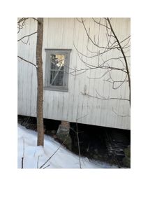 Fotografi av en hvit, trepanelert bygning med et vindu, hevet over snødekt terreng.