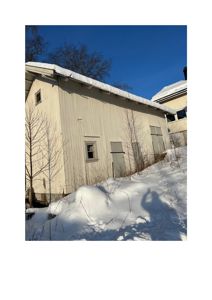 Fotografi av en hvit, trepanelert bygning med snø på taket og på bakken.