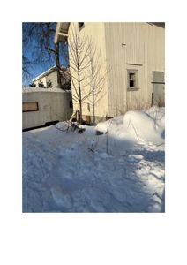 Fotografi av en hvit trehusfasade med snø på bakken og en campingvogn i bakgrunnen.