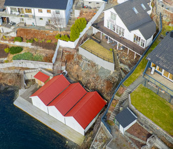 Luftfoto av en bygning med rødt tak og en kai ved vannet, sett fra en høyde.