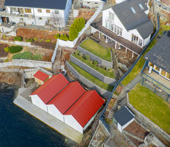 Luftfoto av en boligbebyggelse langs kysten, med fokus på et nytt bygg med rød tak og omgivende tomter.