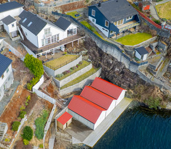 Luftfoto av en kystnær bebyggelse med flere hus og en stor båthall ved vannet.