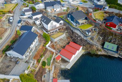 Luftfoto av et boligområde langs kysten med flere hus, veier og natur.