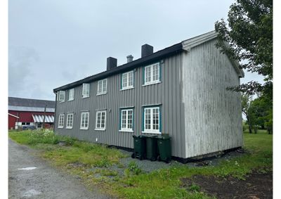 Fotografi av en lang, toetasjes bygning med grå fasade og hvite vinduer, sett fra en vinkel som viser både front og side.