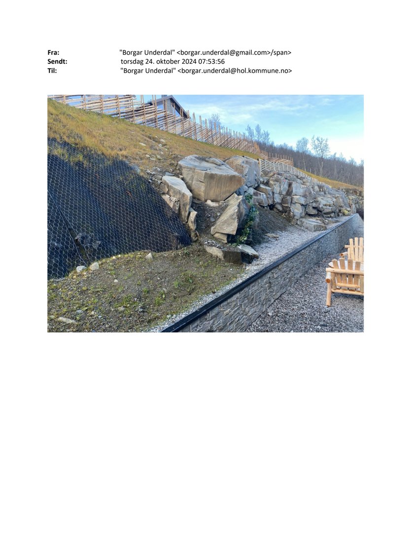 Fotografi av en steinmur, en hekk og en skråning med en bygning i bakgrunnen.