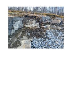 Fotografi av en steinmur eller bergvegg med løse steiner foran, sannsynligvis i et byggefelt eller naturmiljø.