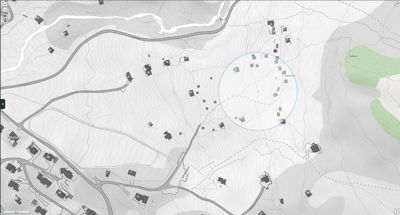 Kart over et område med topografi, veier og flere bygninger. En blå sirkel markerer et spesifikt område med flere hus.