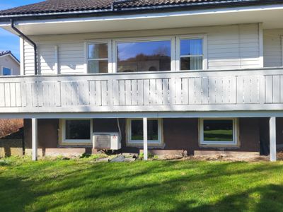 Fotografi av fasaden på en toetasjes bolig under ombygging eller vedlikehold. Bildet viser etasjeforskjell, balkong, vinduer og en luftkondisjonsenhet.