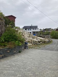 Fotografi av en eksisterende eller planlagt bygning sett fra en vei eller parkeringsplass, med omgivende natur og nabolag.