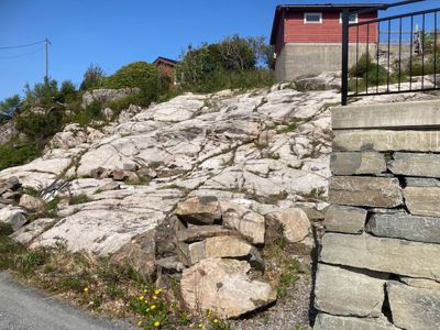 Fotografi av en steinete bakke med en rød bygning i bakgrunnen og en steinmur i forgrunnen.
