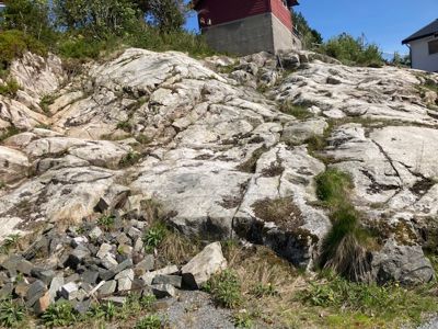 Fotografi av et steinete terreng med en rød bygning i bakgrunnen.