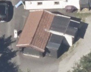 Luftfoto (satellittbilde) som viser en bygning med tak, plassert på en tomt med bilplassering og omgivende beplantning.