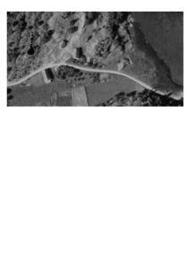 Flyfoto eller satellittbilde som viser et landskap med en vei, noen bygninger og kystlinje.